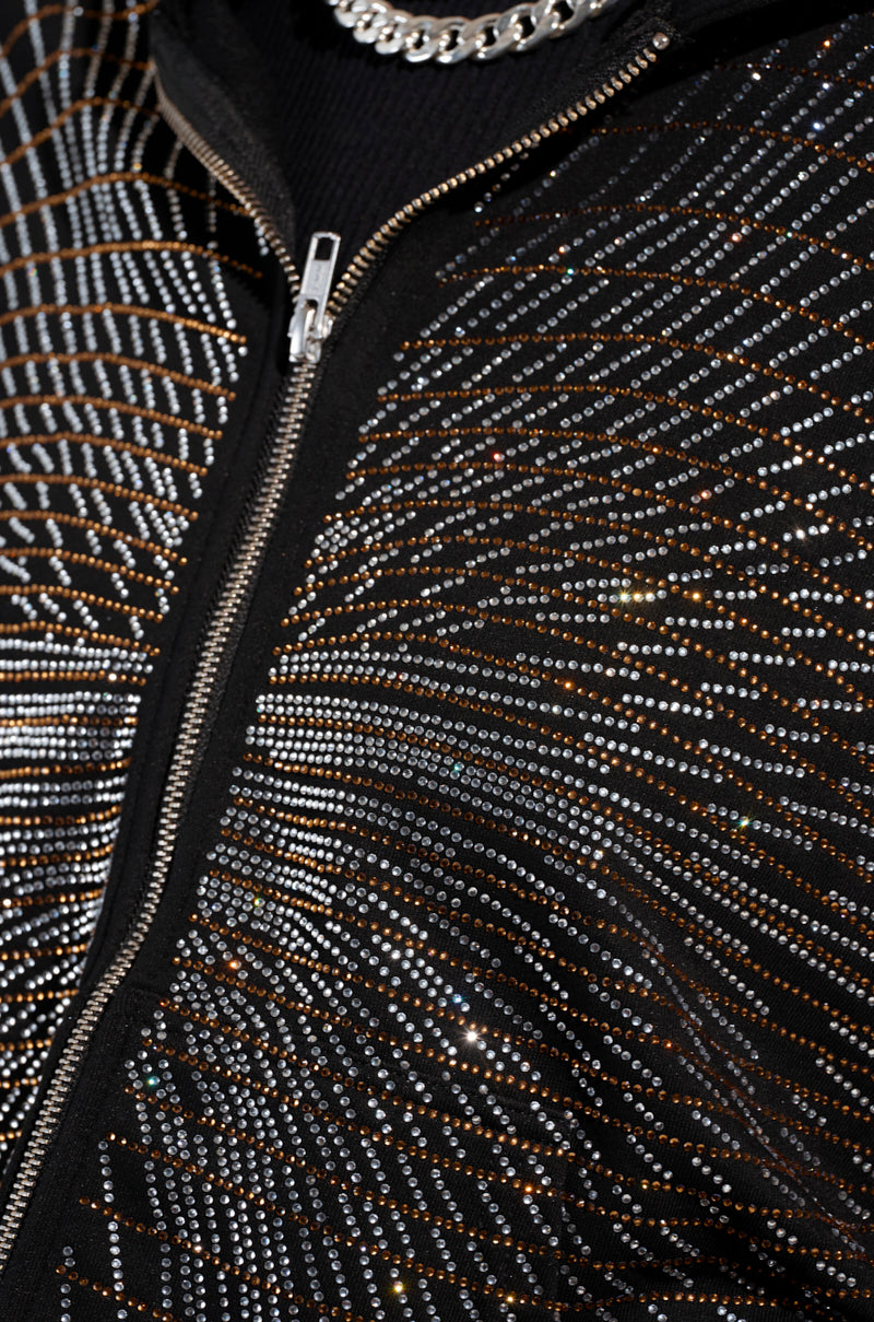 A close-up of the "LIGHTS, CAMERA, ACTION! EMBELLISHED ZIP UP SWEATSHIRT" showcases its intricate patterns adorned with shining silver and gold rhinestones. Visible at the top is a silver chain necklace that enhances the dynamic, shimmering effect complementing its oversized silhouette.