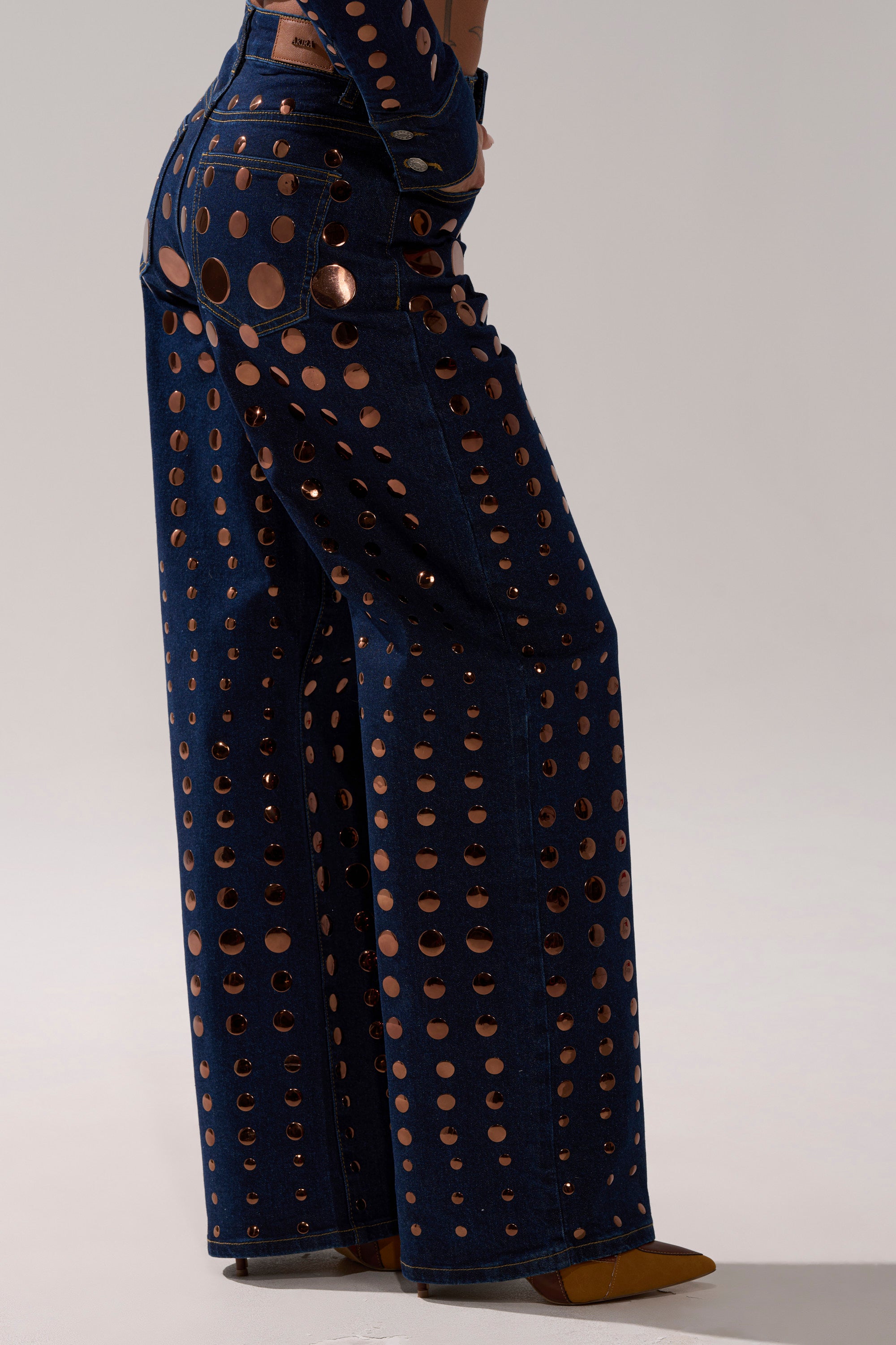 A woman wearing DISCO BABE RELAXED DENIM, high-waisted pants featuring blue and gold polka dots.