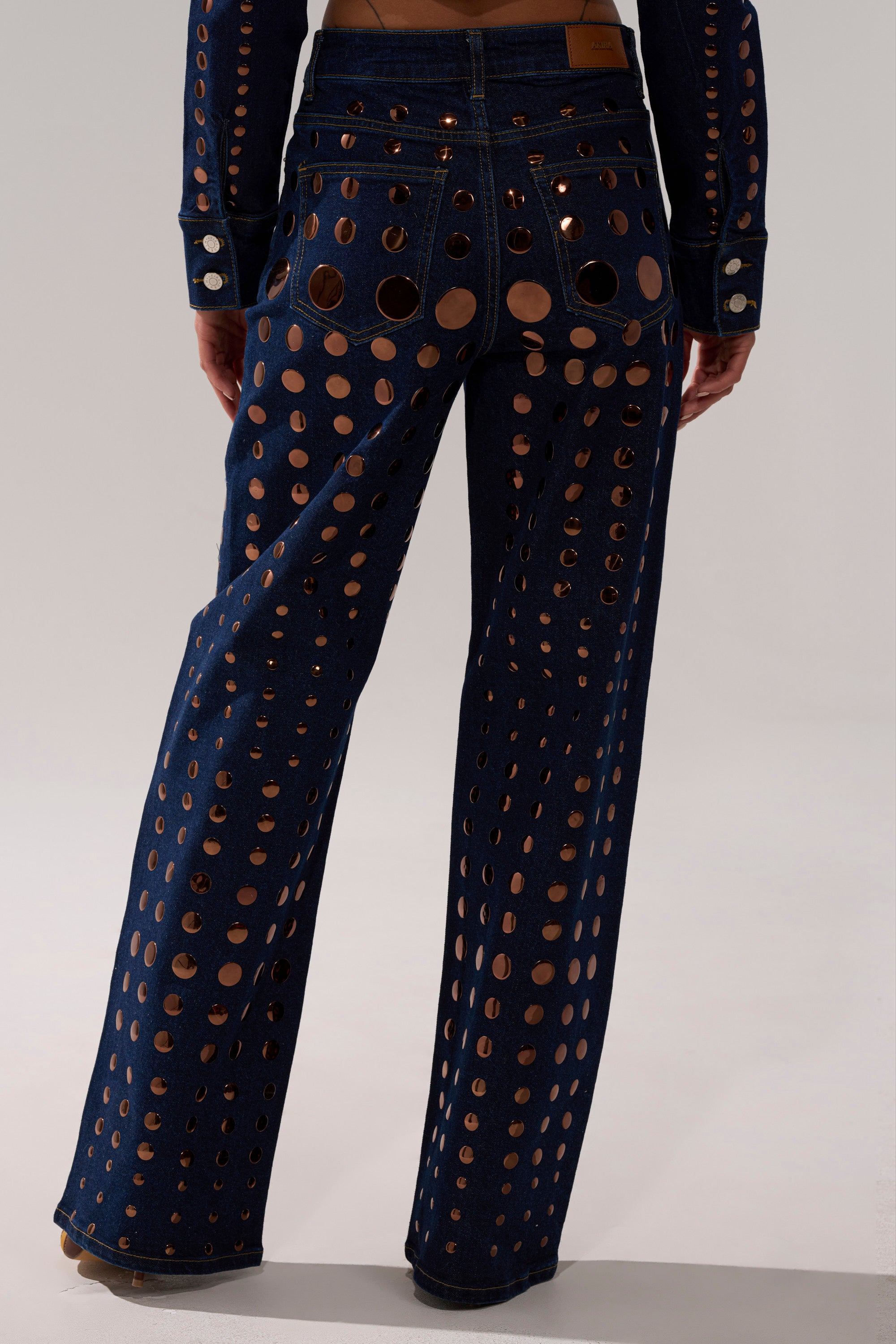 Wearing the DISCO BABE RELAXED DENIM, which features high-waisted, wide-leg jeans with bold circular cutouts and visible back pockets. Photo taken from behind highlights this statement design's unique style.