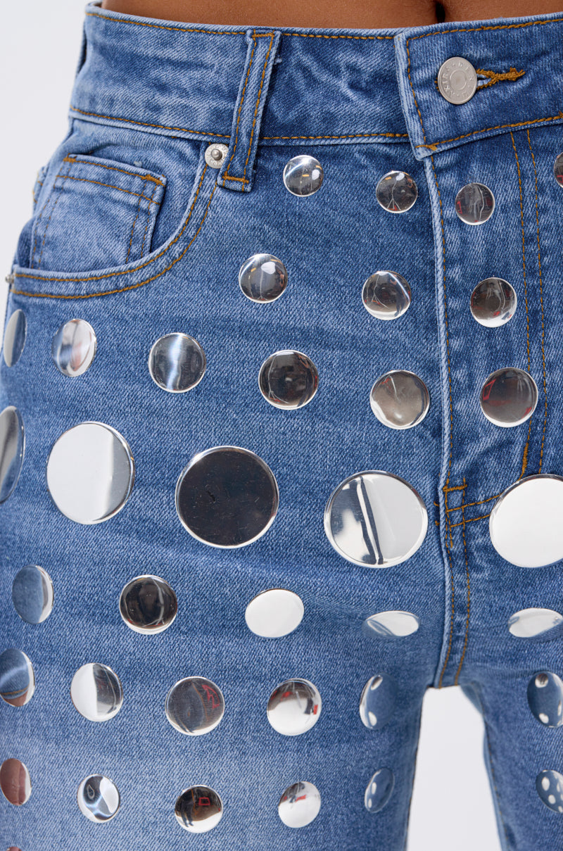 Close-up of the STUDS EVERYWHERE RELAXED DENIM PANT, featuring relaxed high-rise denim adorned with shiny, round silver studs, visible stitching, belt loops, and a metal button.