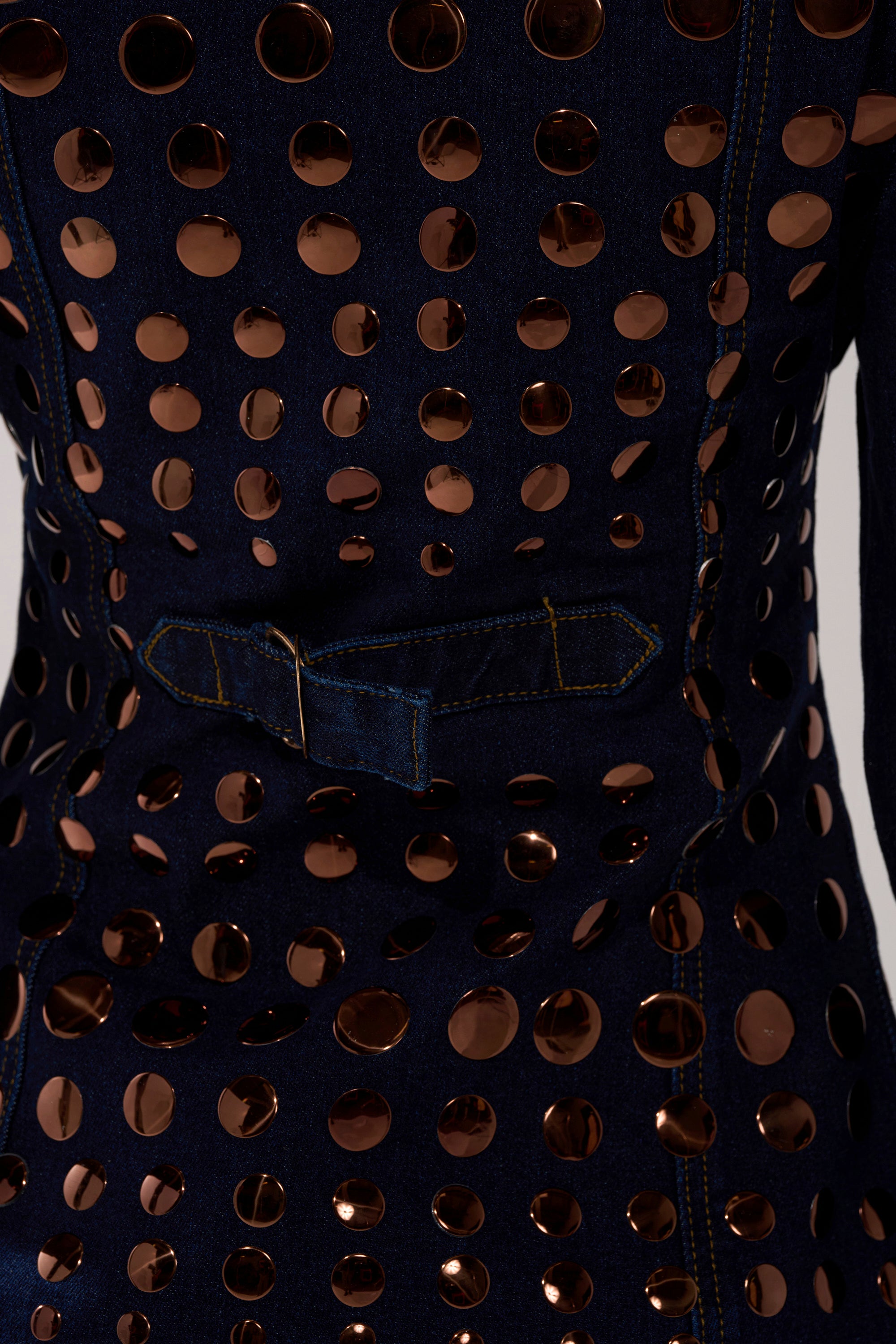 Close-up of the DISCO BABE DENIM BUTTON DOWN in dark-wash denim, featuring gold circular mirrored embellishments in rows, visible yellow stitching, and a waist denim belt.
