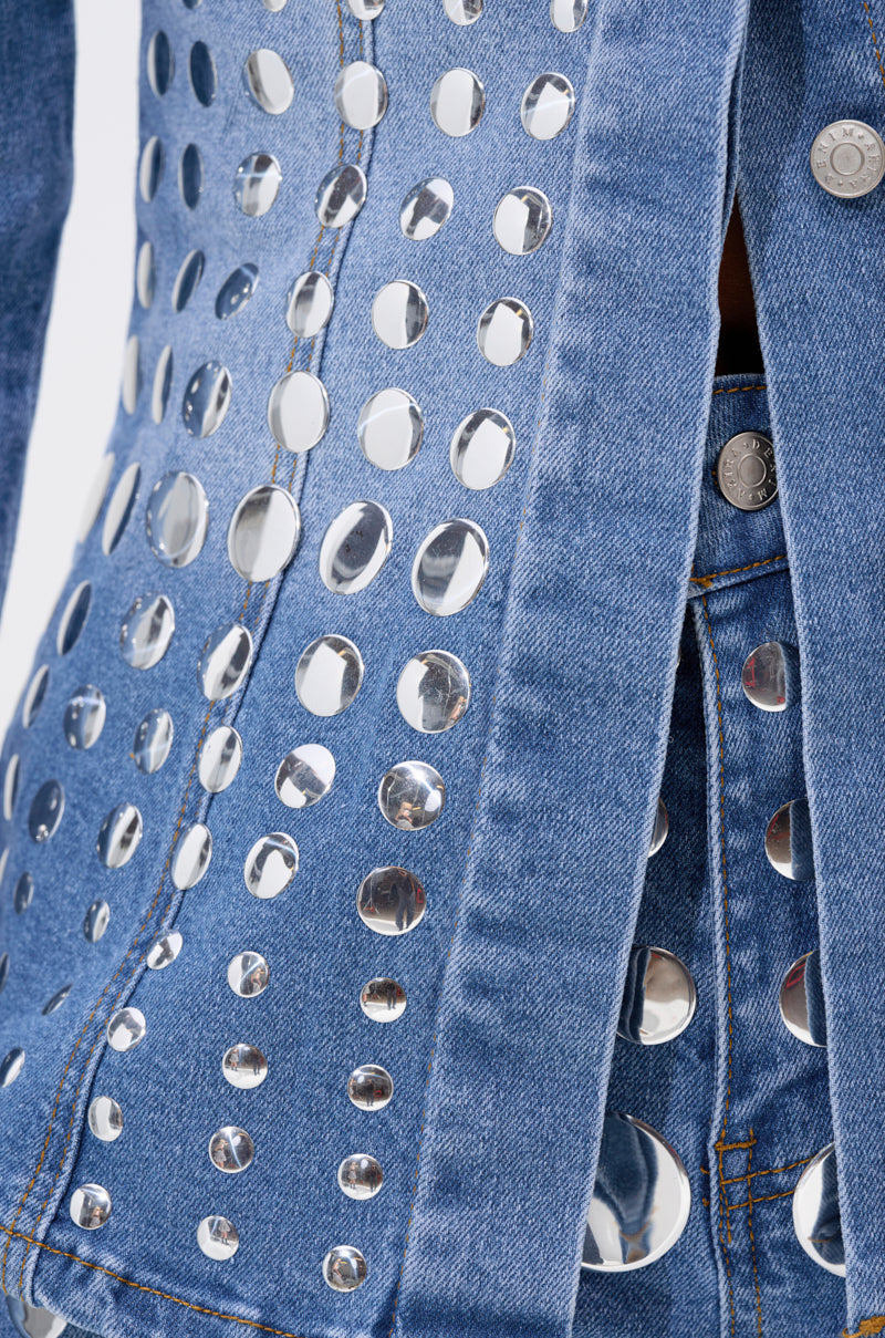 Close-up of the STUDS EVERYWHERE BUTTON DOWN, a blue denim top adorned with shiny, round silver studs that create a reflective, patterned texture.