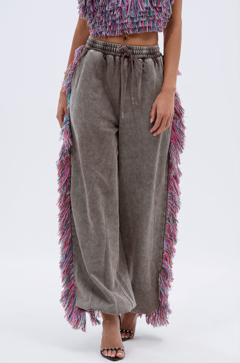 A person wears THE ONE WIDE LEG JOGGER WITH FRINGE—featuring colorful side trim—with a matching textured crop top and open-toe heels, creating a stylish and playful look.