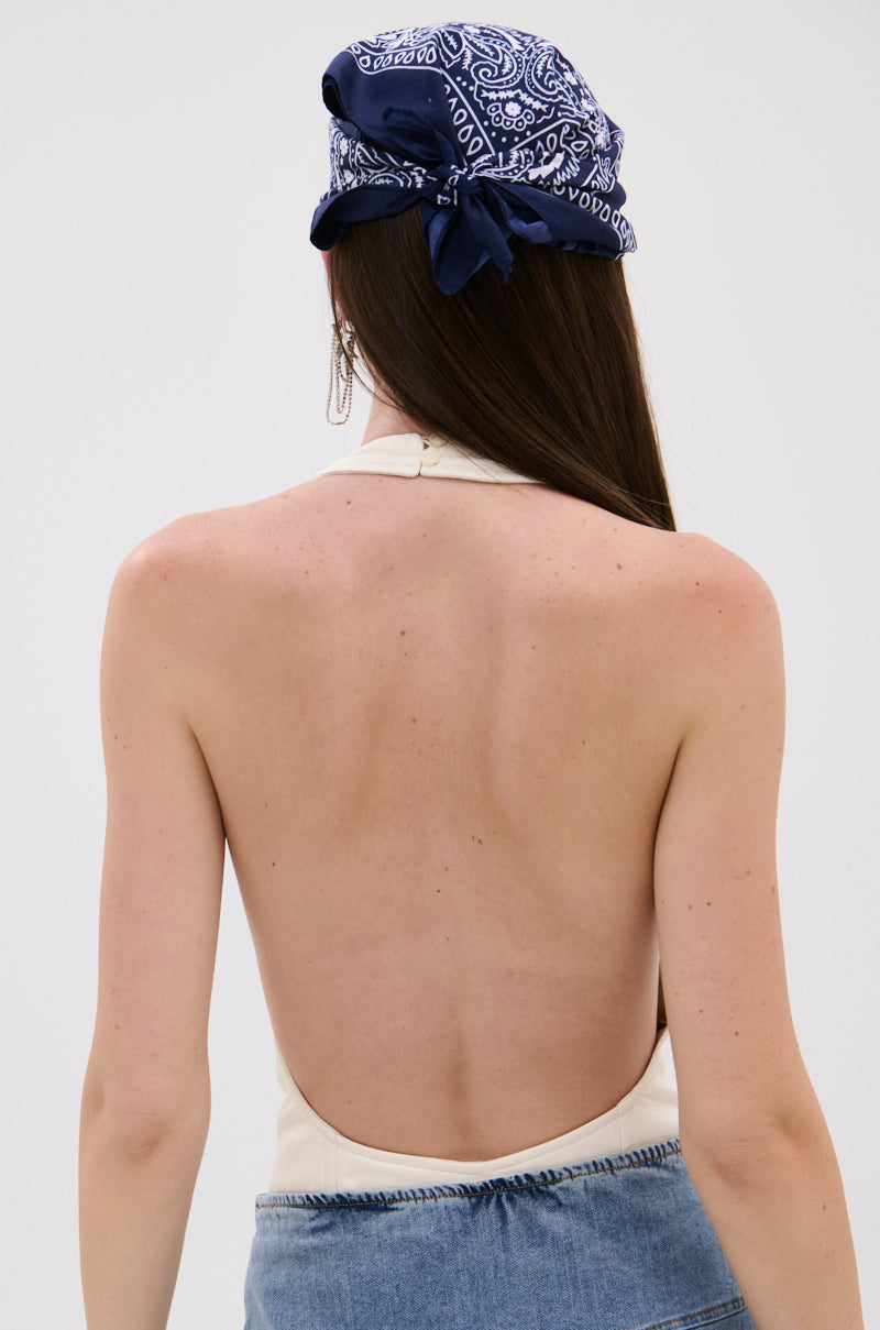 A woman with long brown hair wears the SEXY THANG BODYSUIT, featuring a blue paisley bandana and curve-hugging lace-up halter style, paired with blue denim bottoms. She stands with her back to the camera. 4