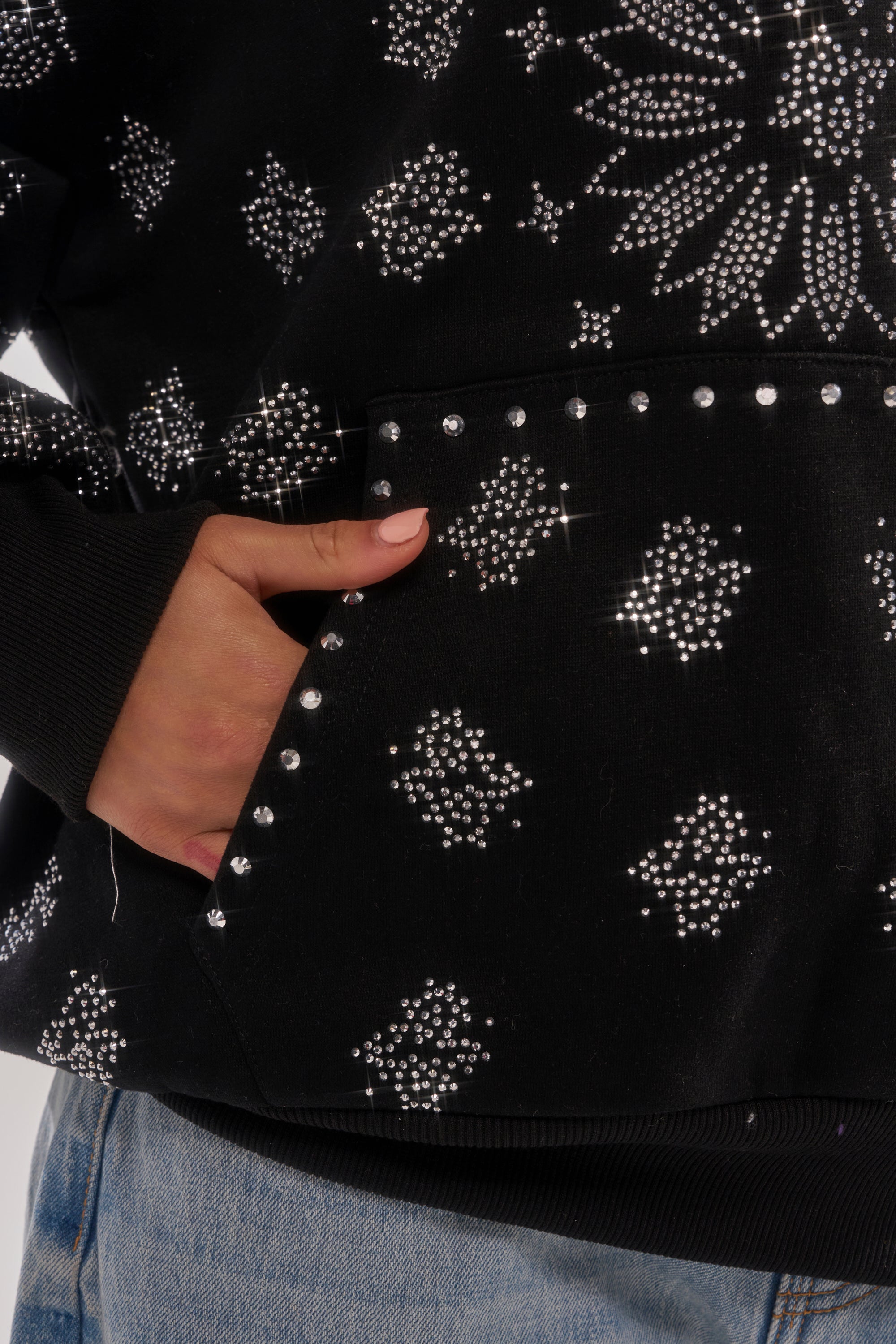 Wearing the FEELING FREE SWEATSHIRT—a black hoodie with sparkling floral and geometric rhinestone designs—paired with light blue jeans, this streetwear look blends bold style and comfort, with a hand casually slipped into the front pocket. 8