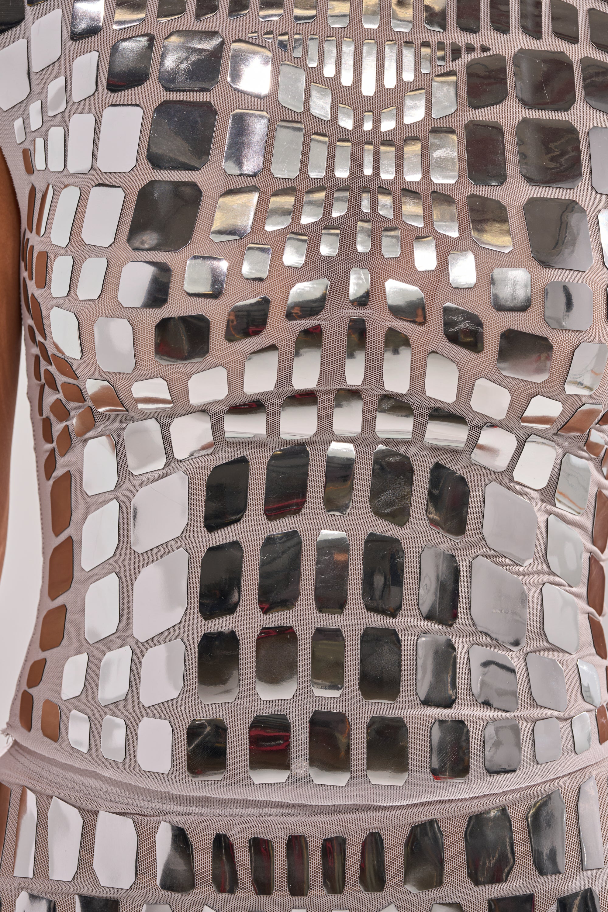 A close-up of a person wearing the CHAMPAGNE POPPIN BLOUSE, featuring square and rectangular mirrored tiles that form a reflective, mosaic-like pattern on beige fabric.