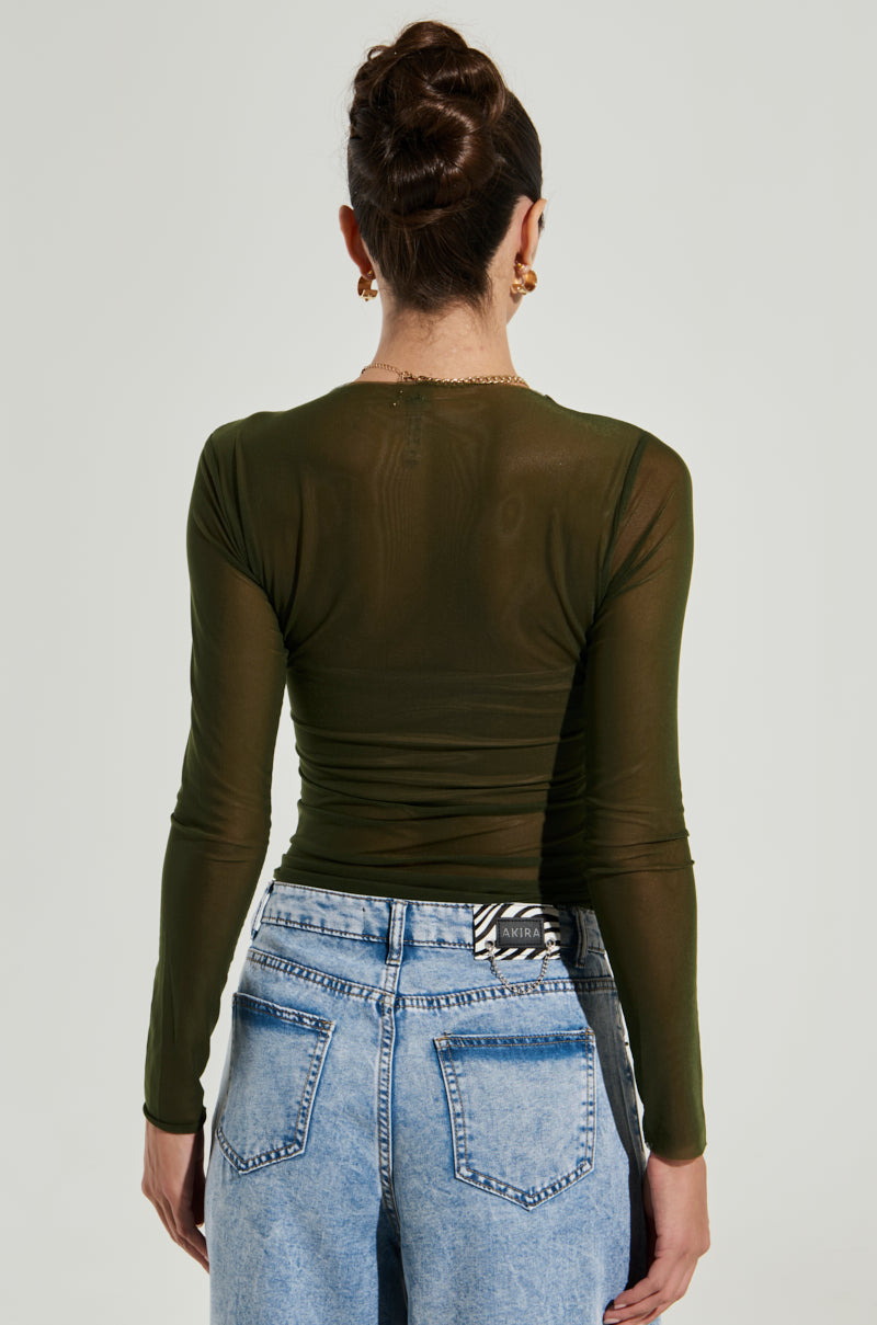 A person with an updo hairstyle is seen from behind, wearing the Paxton Raw Hem Long Sleeve Mesh Tee in Olive and light blue high-waisted jeans with back pockets. The background is plain and light-colored.