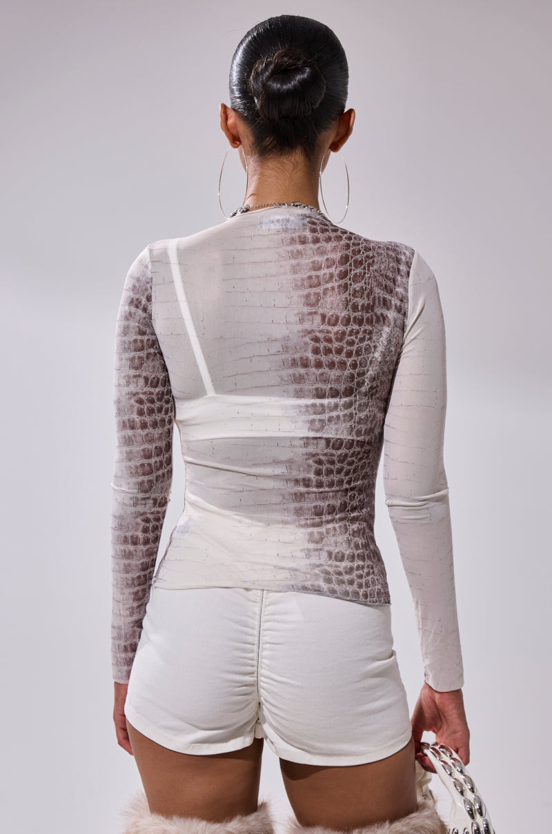 Seen from the back, a person with a sleek bun wears the ELBA PYTHON LONG SLEEVE MESH TOP and white high-waisted shorts, paired with large hoop earrings and a white bag.