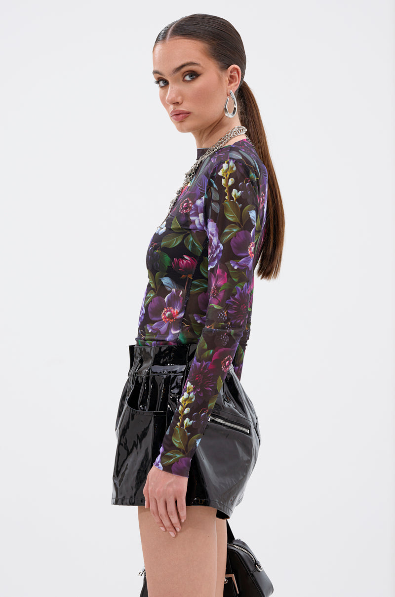 A woman with a sleek ponytail models the ANOTHER ROSE LONG SLEEVE MESH TOP and shiny black vinyl shorts, standing in profile and gazing at the camera against a neutral background. 3