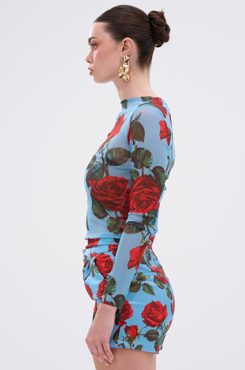 A woman in profile wears the DOZEN ROSES MESH TOP with a pop art floral print, paired with matching shorts, gold statement earrings, and a sleek bun hairstyle against a plain light backdrop.