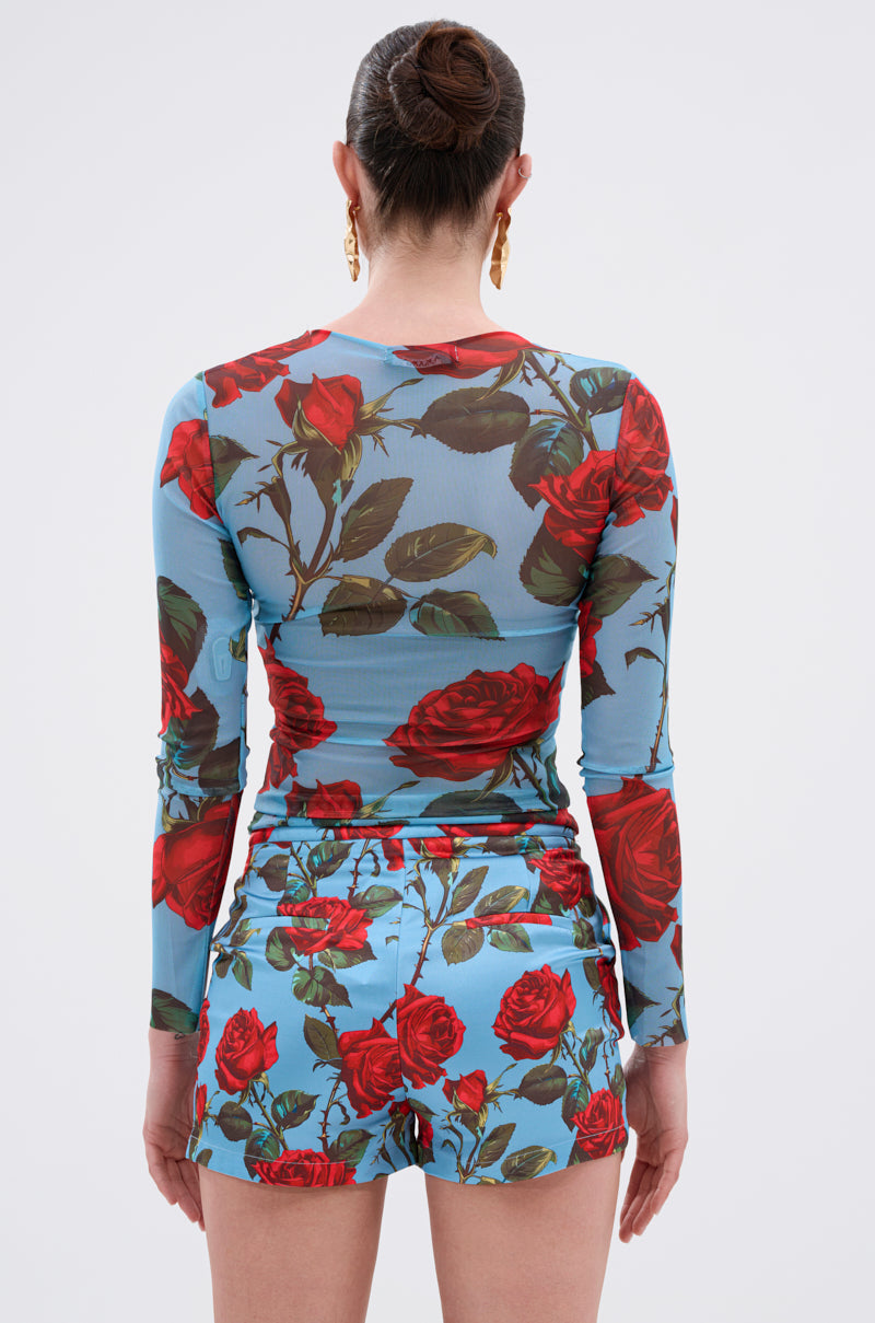 A person with dark hair in a bun, gold hoop earrings, and the DOZEN ROSES MESH TOP with matching bold floral shorts is shown from behind against a plain light background.