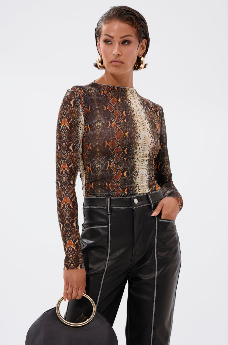 A woman with short hair and large hoop earrings wears the SNAKE VIBES MESH TOP with high-waisted black leather pants, holding a round black handbag with a gold handle.