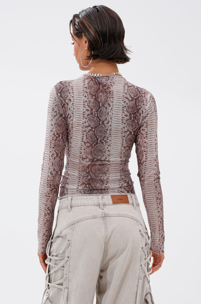 A person with short dark hair and large hoop earrings wears the SNAKE CHARMER LONG SLEEVE MESH TOP, a necklace, and light gray lace-up side pants, standing with their back to the camera.