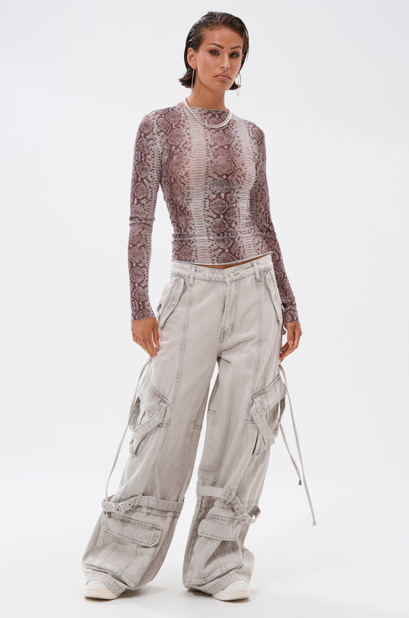 A person stands confidently wearing the SNAKE CHARMER LONG SLEEVE MESH TOP and baggy, light gray cargo pants with drawstring details, set against a plain white background.