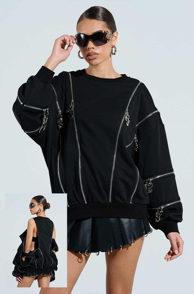 A woman models an oversized silhouette with the UNZIP ME SWEATSHIRT featuring a silver metallic zipper and a leather mini skirt. An inset image shows its open-back design, while she exudes sleek style with slicked-back hair and oversized sunglasses.
