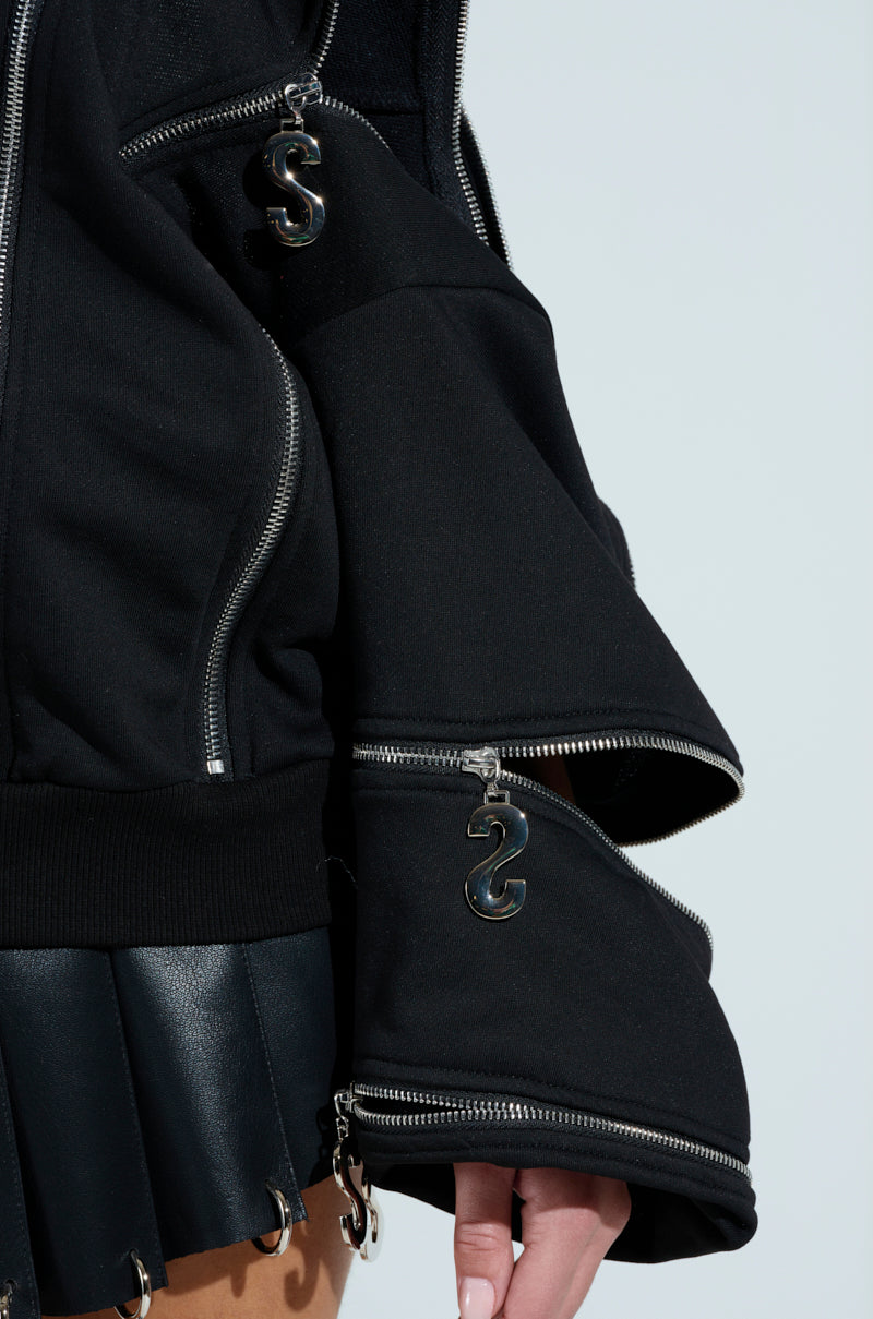 A close-up shows someone in the UNZIP ME SWEATSHIRT, featuring a black oversized design with silver metallic zippers and "S" pulls. It's paired with a black pleated skirt accented with metal, revealing a small part of their hand.