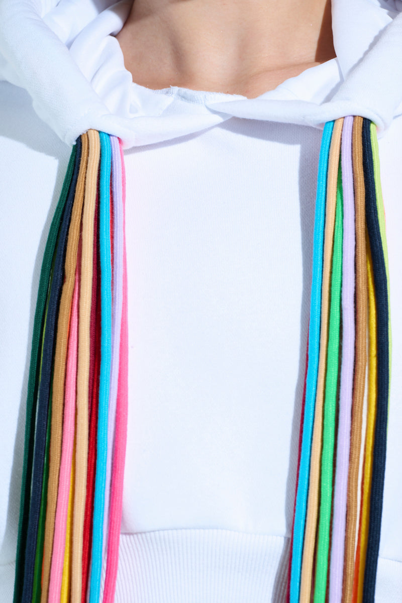 A person wearing the STRINGED HOODIE, showcasing adjustable drawstrings in vibrant pink, blue, green, yellow, and black against a plain cropped sweatshirt.