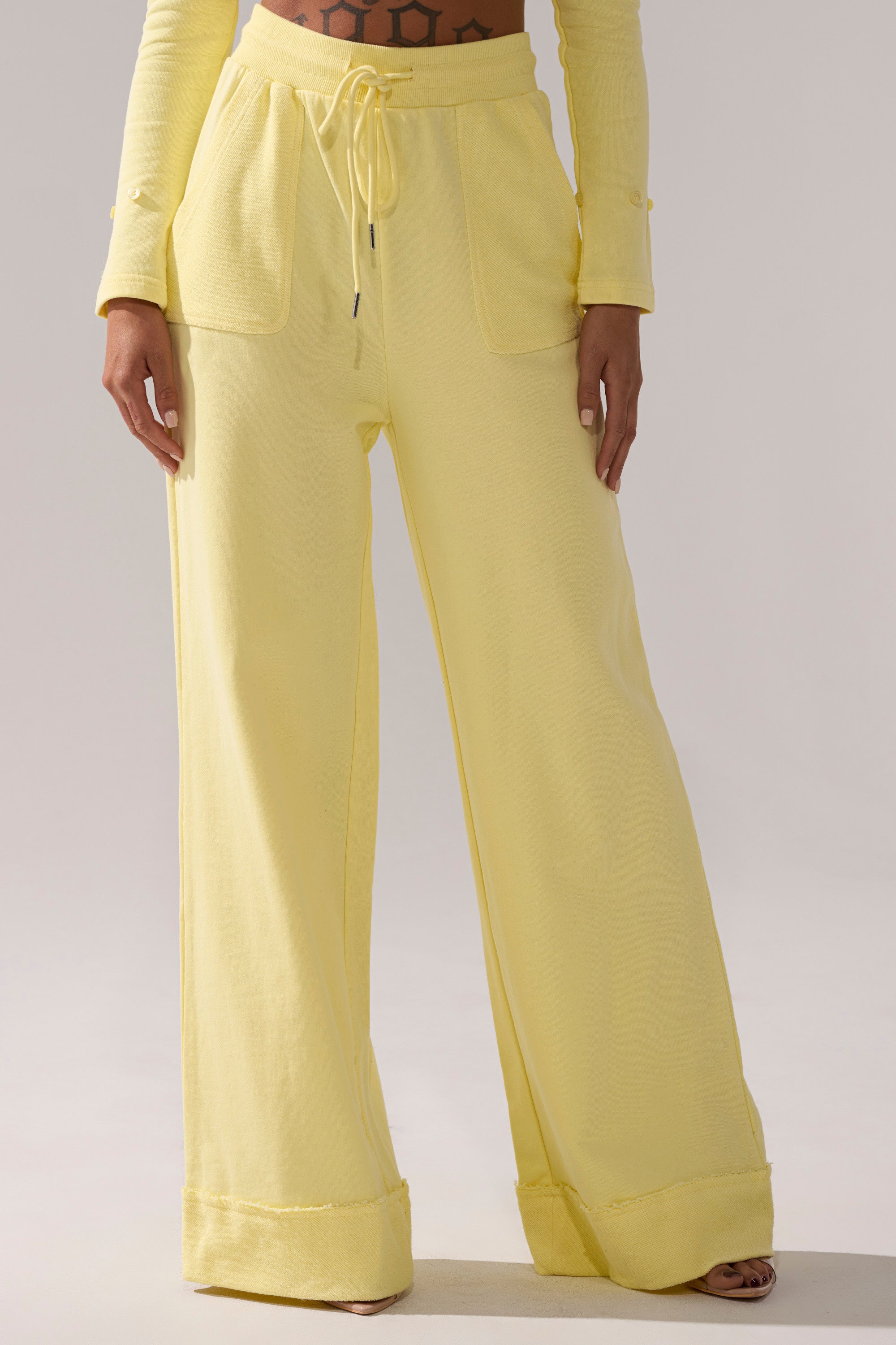 A person wears BUTTERFINGER WIDE LEG SWEATPANT, high-waisted with front pockets and a drawstring waist, styled with a matching long-sleeve crop top.