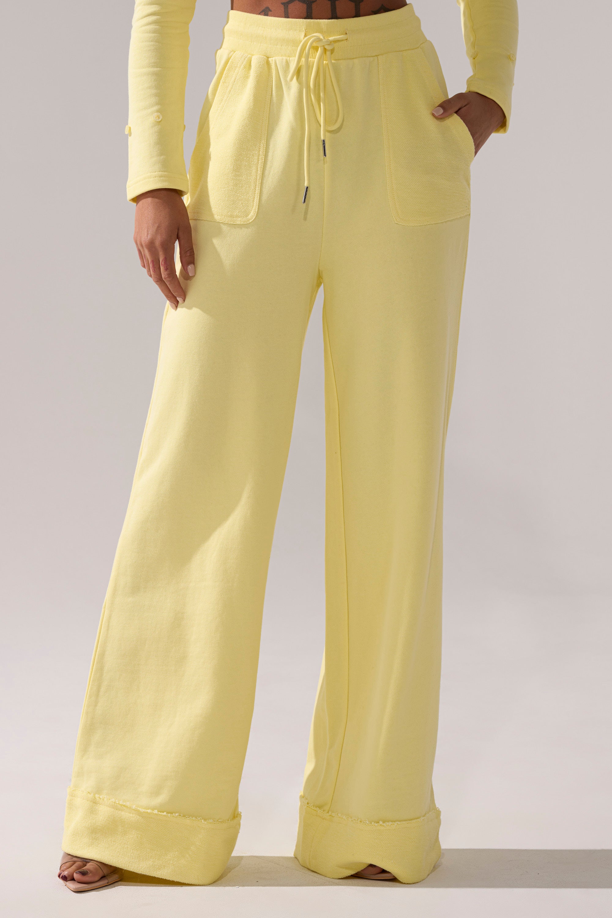 A person wearing the BUTTERFINGER WIDE LEG SWEATPANT—high-rise, wide-leg yellow cotton pants with front pockets and a drawstring waist—paired with a matching yellow long-sleeve top for a relaxed, comfortable fit.