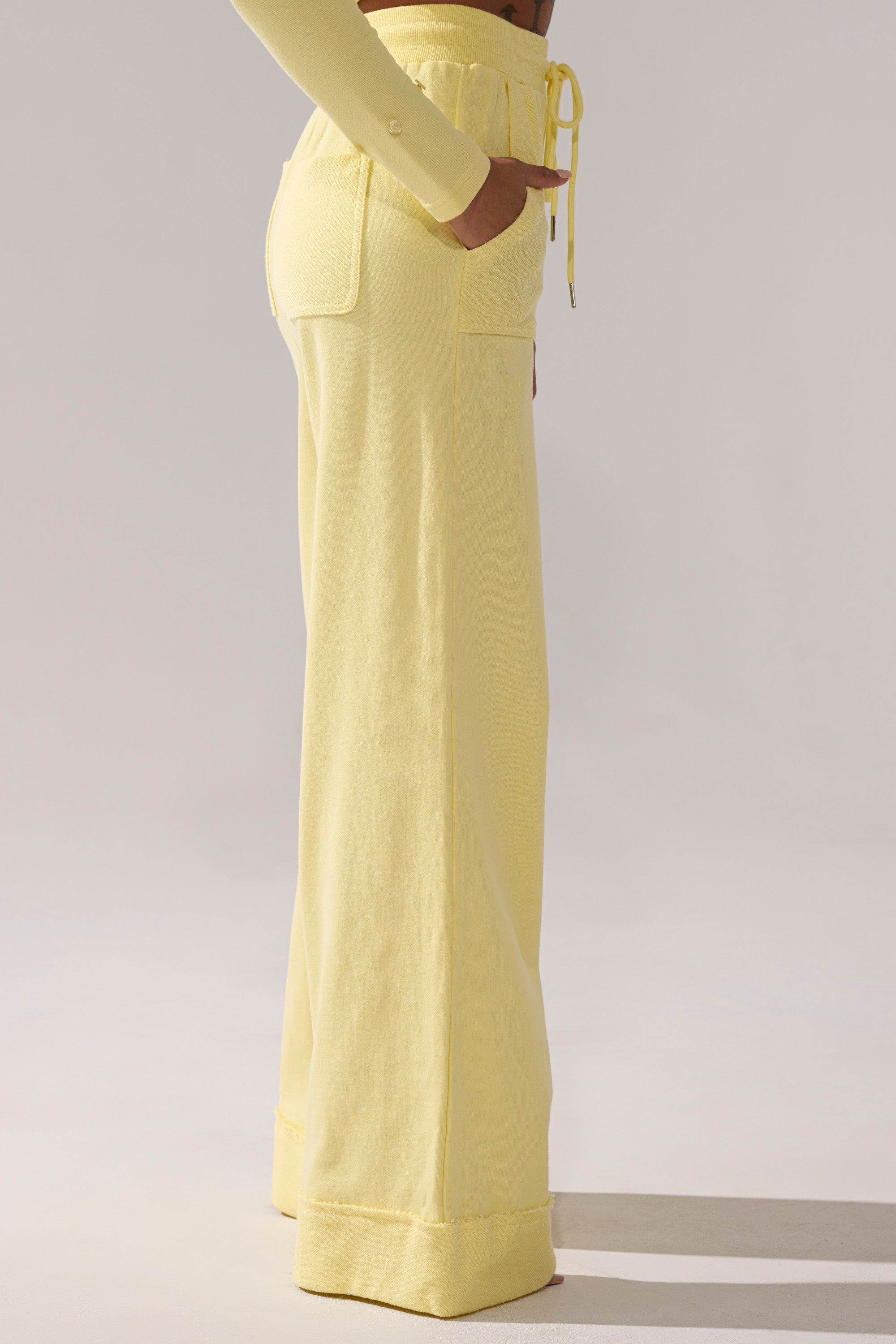 Someone stands sideways against a neutral background, one hand in their pocket, wearing the BUTTERFINGER WIDE LEG SWEATPANT featuring a high waist, wide legs, patch pockets, and a drawstring waist.