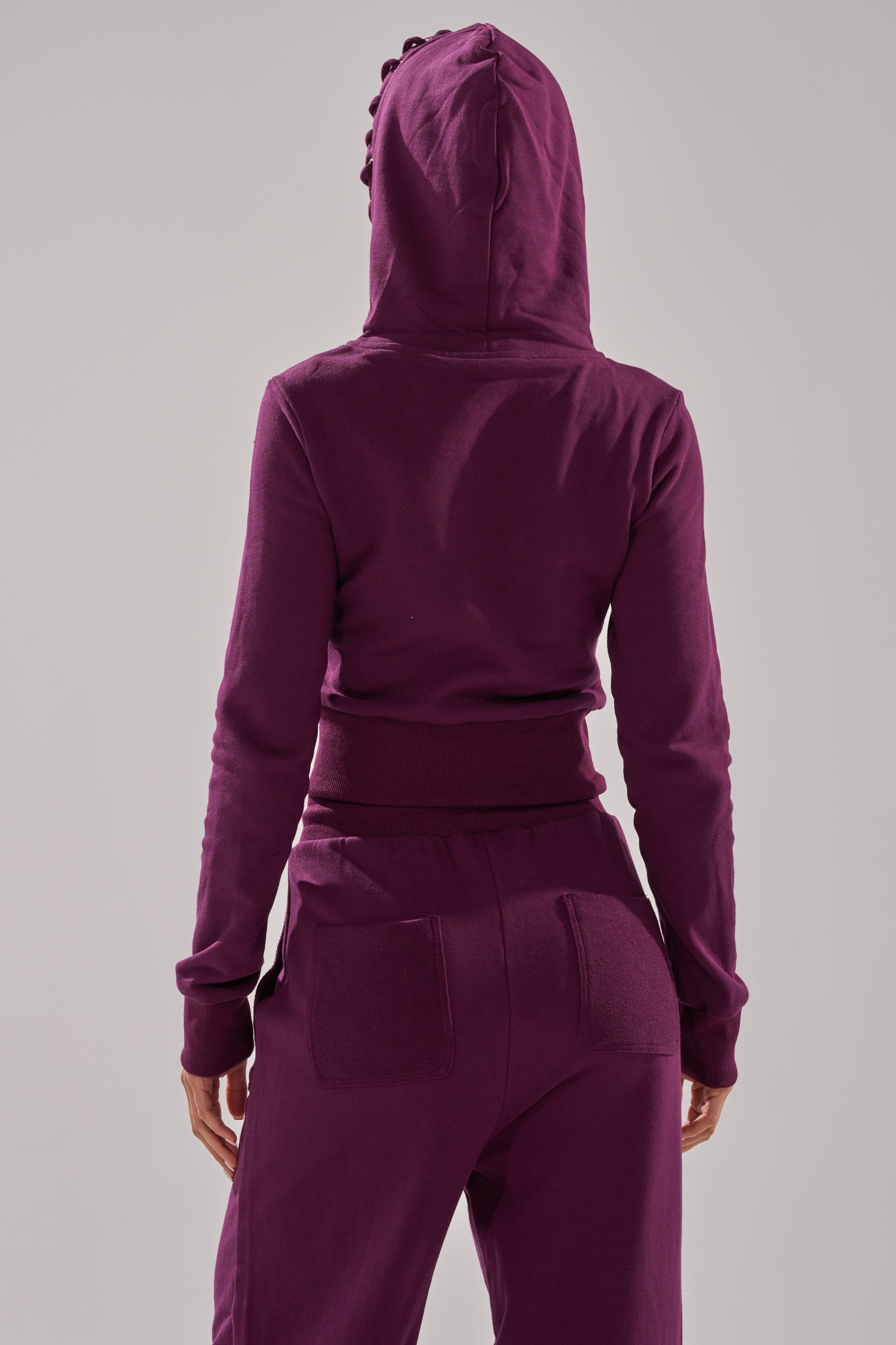 Someone wearing a dark purple SHE'S GONE, YOU'RE FINE ZIP UP SWEATSHIRT with matching sweatpants stands with their back to the camera against a plain light background. 7