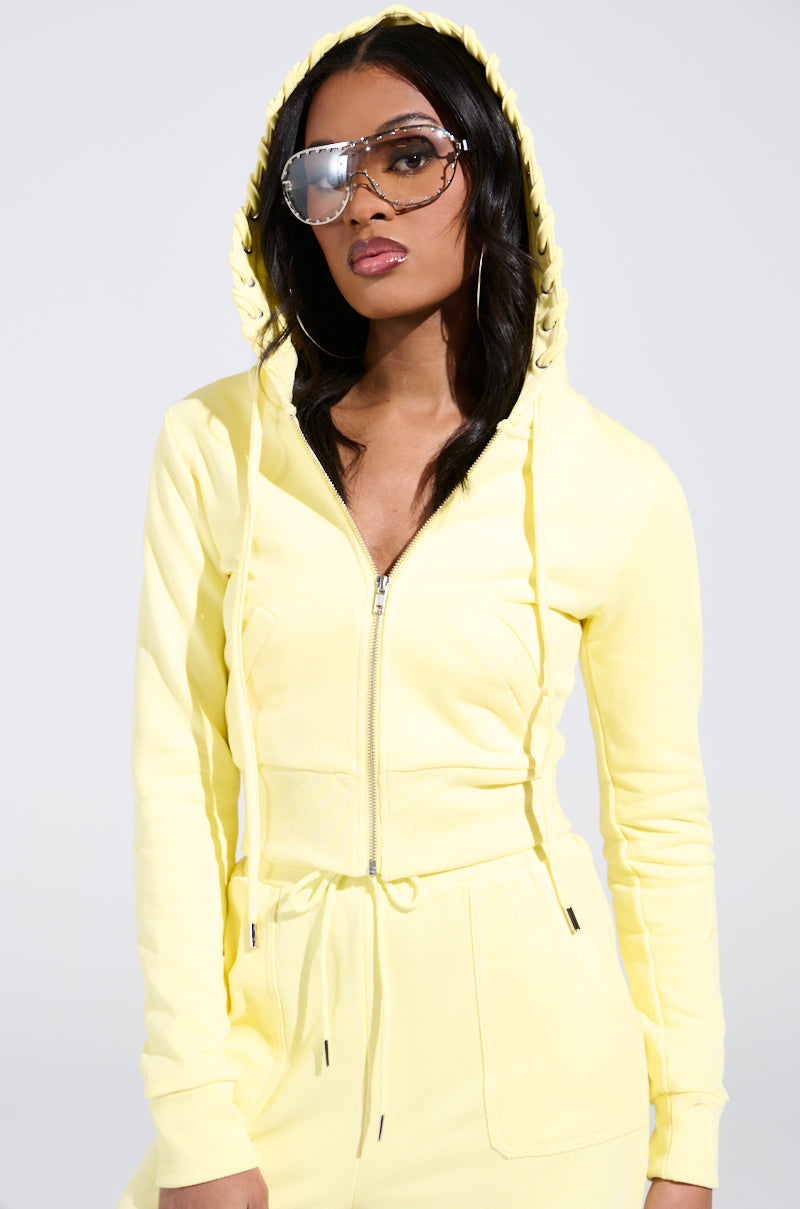 Wearing a vivid yellow BUTTERFINGER SWEATSHIRT with the hood up, large reflective sunglasses, and hoop earrings, a person stands out against a plain light gray background for a striking monochromatic look.