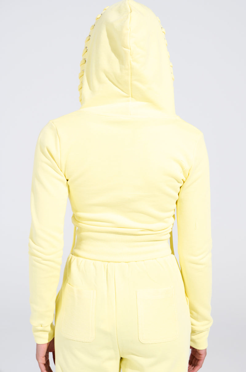 A person in a vibrant yellow BUTTERFINGER SWEATSHIRT tracksuit with the hood up showcases a monochromatic look, including long sleeves and pocketed pants, set against a plain white background.