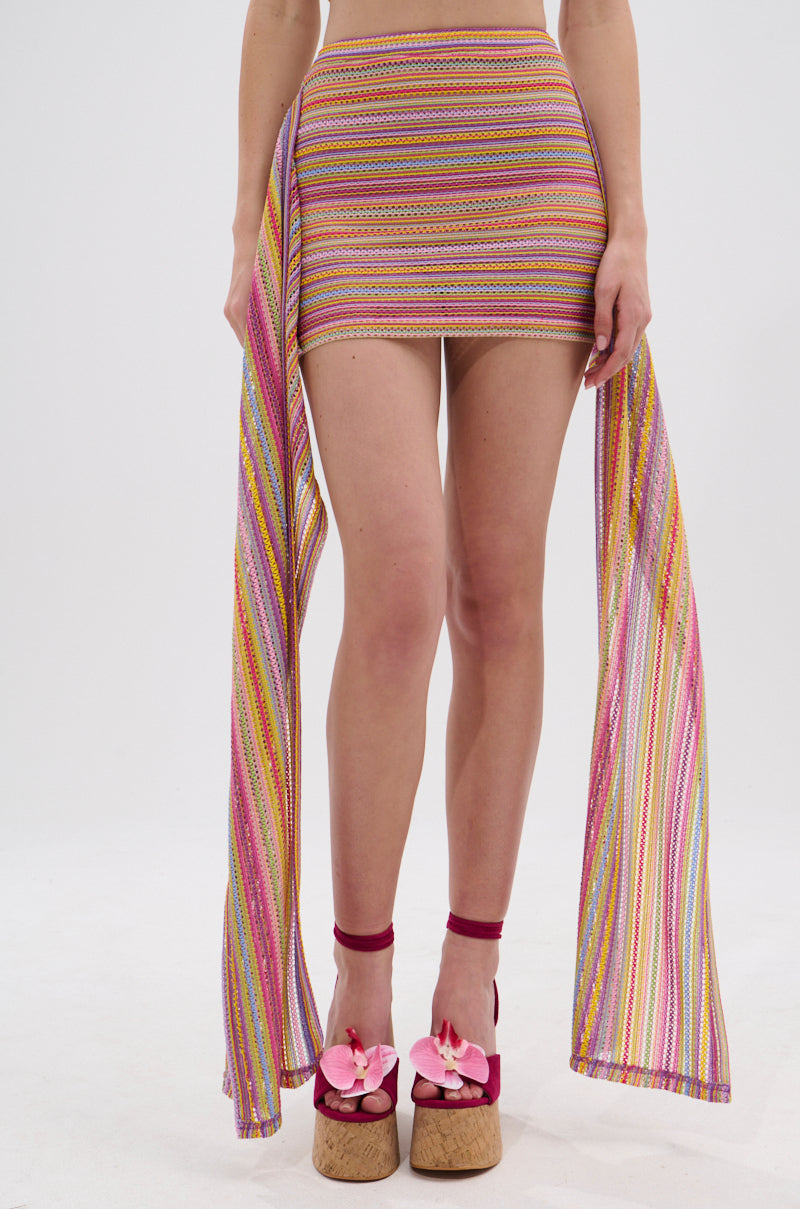 A person wearing the MORNING SHINE CROCHET MINI SKIRT with long, matching side panels and platform sandals with pink bows, standing against a plain white background. 2