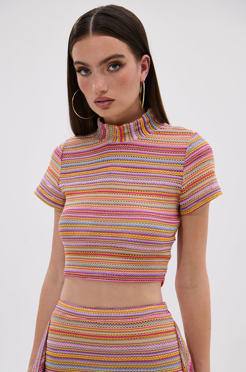 A woman with long brown hair and large hoop earrings wears the MORNING SHINE CROCHET SHORT SLEEVE CROP TOP and a matching high-waisted skirt against a plain light background. 1