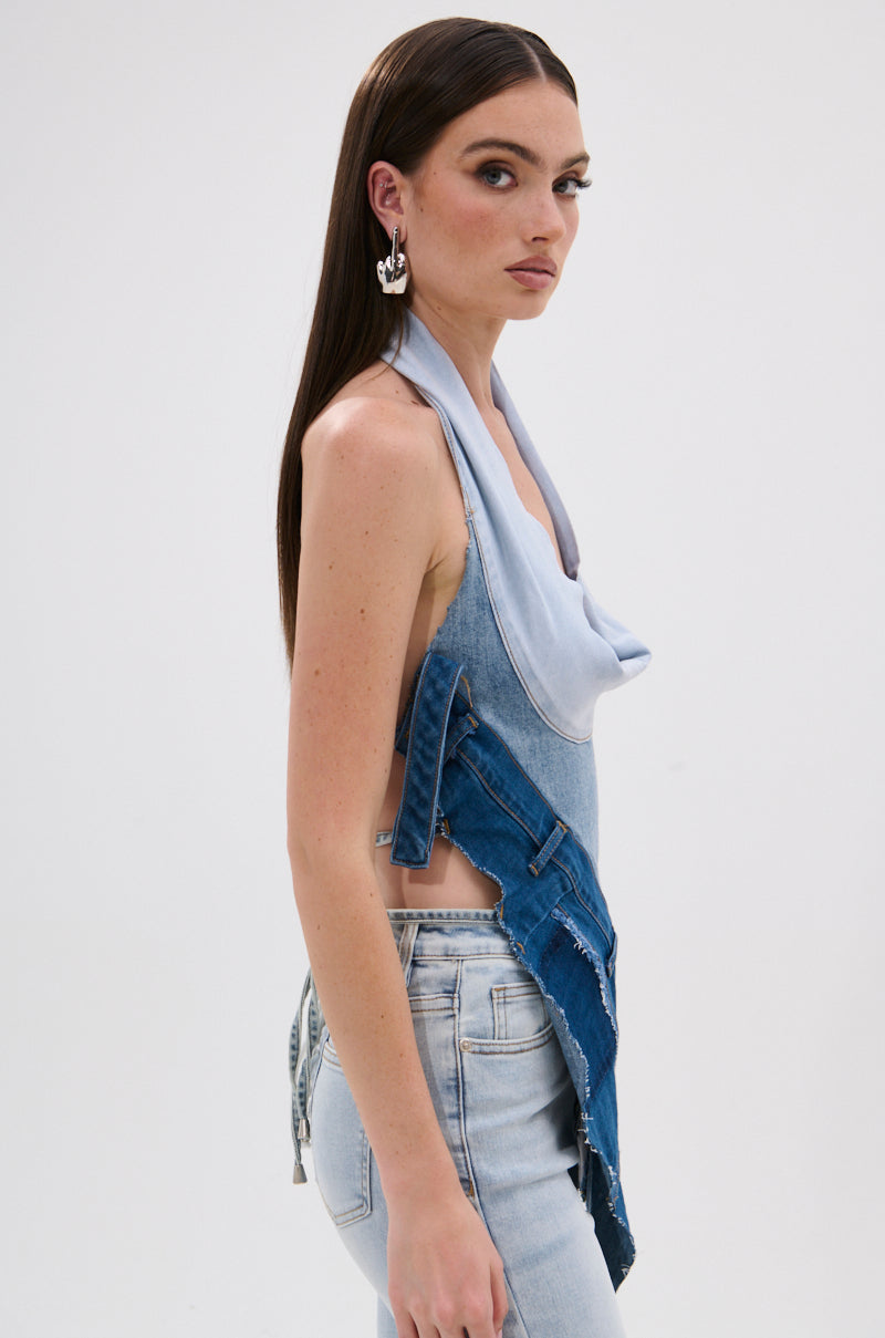 A woman with long straight hair models the PATCHED UP COWL NECK DENIM HALTER TOP in light blue patchwork style, paired with light-washed jeans and silver earrings. She stands sideways against a plain white background, channeling Y2K vibes. 3