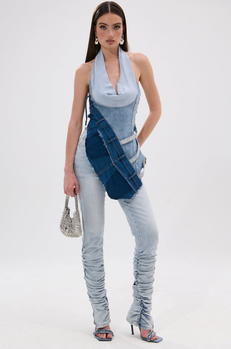 A woman in light-wash ruched jeans, heeled sandals, and the PATCHED UP COWL NECK DENIM HALTER TOP holds a small beaded handbag. With straight long dark hair and bold makeup, she channels Y2K fashion against a plain white background. 5