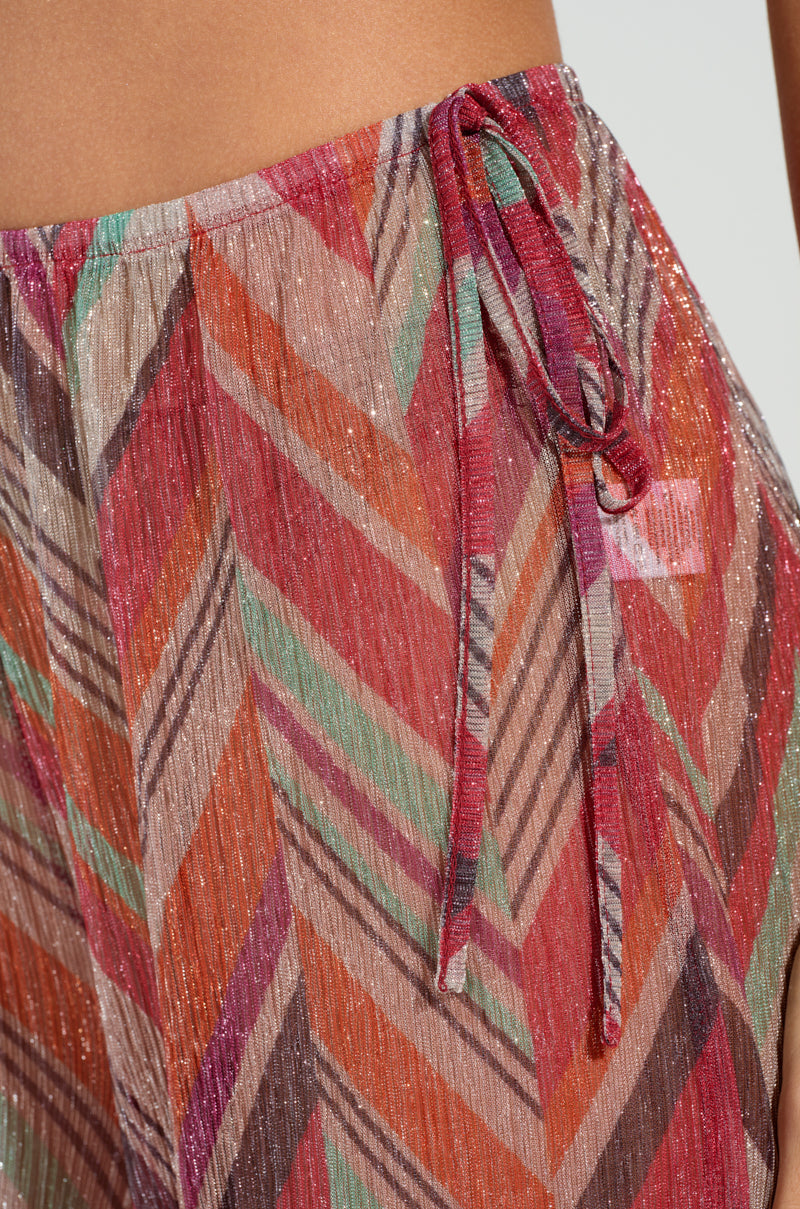 Close-up of the CALI FAYE WIDE LEG PANT, featuring a vibrant chevron pattern in red, orange, pink, green, and silver. The pants have a textured look with a drawstring and an elasticized waistband.