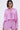 A woman with a sleek bob and glasses wears the TAKE ME TO IBIZA TIE FRONT TOP, a pink and purple striped blouse, paired with matching high-waisted shorts, posing against a plain light background.