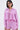 A woman models the TAKE ME TO IBIZA TIE FRONT TOP in matching pink and purple vertical stripes, paired with coordinating shorts, silver hoop earrings, and blue rectangular sunglasses, set against a plain white background.
