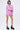 A woman wearing the TAKE ME TO IBIZA TIE FRONT TOP stands confidently. She has short dark hair, glasses, statement earrings, matching high-waisted shorts, and black platform shoes.