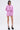 A woman with short dark hair wears the AKIRA Label TAKE ME TO IBIZA TIE FRONT TOP, a pink and white striped blouse, paired with matching shorts. She stands facing forward in black platform heels and glasses against a plain background.