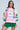 A woman stands confidently in a vibrant NEW YORK BABY SWEATSHIRT with colorful graphics, featuring unique cut-out sleeves for flair. Paired with a green pleated skirt and oversized glasses, the cotton-blend hoodie pops against the solid light blue background.