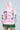 Someone is wearing an oversized pink NEW YORK BABY SWEATSHIRT adorned with patches and prints such as "World Champs," "The World is Yours," and "New York." The sweatshirt, featuring sleeve cut-outs, pairs perfectly with a green pleated skirt.