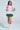 Someone poses confidently in an oversized NEW YORK BABY SWEATSHIRT, featuring a cotton-blend design with "New York" and "World" text. They wear various patches, a green pleated skirt, white boots, and sunglasses against a plain, light background.