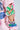 Close-up of a person wearing the NEW YORK BABY SWEATSHIRT, a pink cotton-blend design featuring colorful graphic patches and green, white, and pink cut-out details on the sleeves for a layered look. The background is light blue.