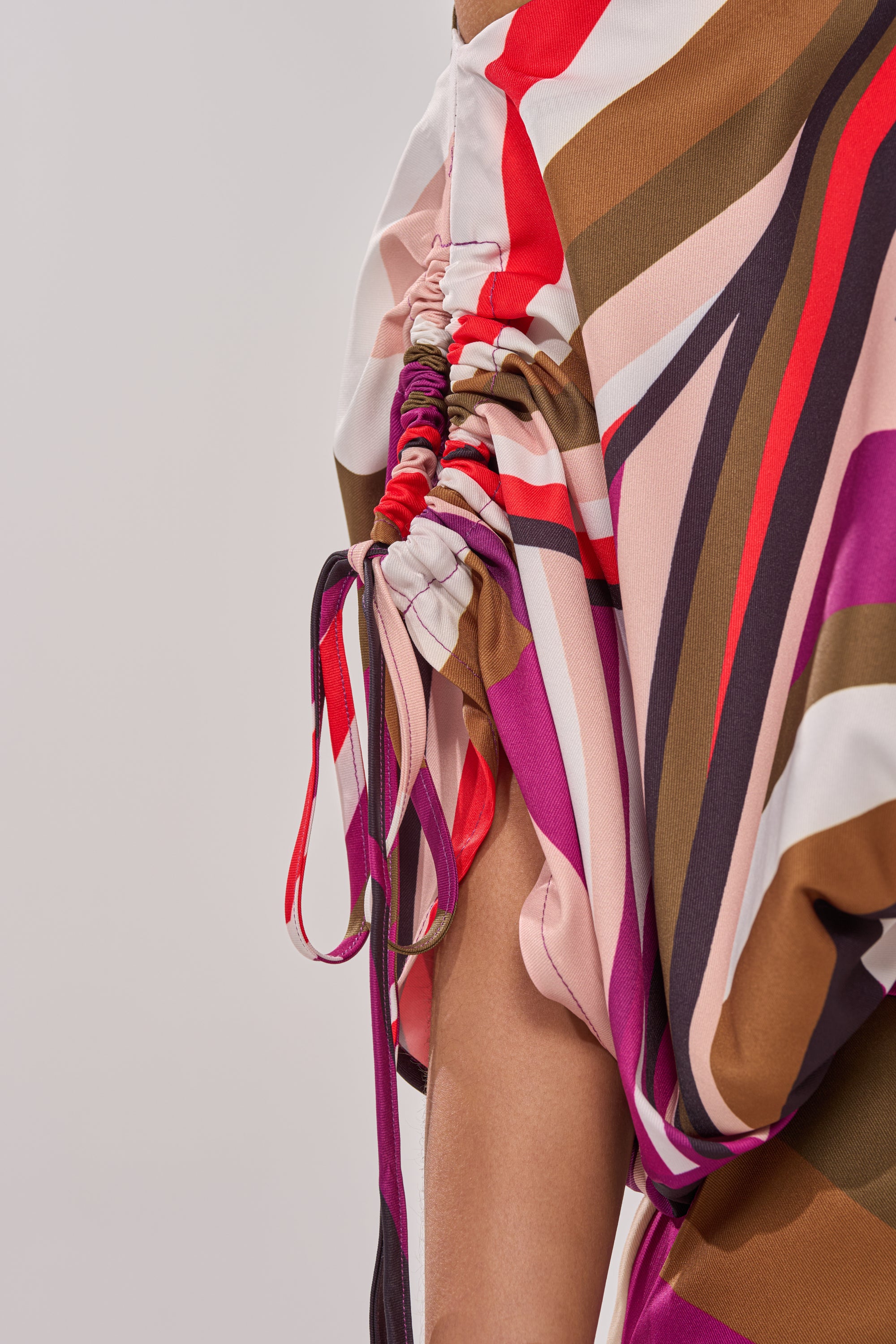 Close-up of the CRAZY IN LOVE OFF THE SHOULDER BLOUSE, a colorful retro top with red, pink, brown, and white stripes, featuring gathered ruching and side tie strings. 10