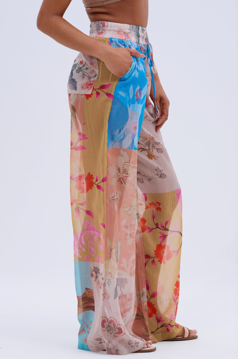 A person wearing the LILY CHIFFON WIDE LEG PANT, showcasing colorful floral patchwork, pockets, and subtle color-blocking, is photographed from the side against a light background—a perfect resort-ready look.