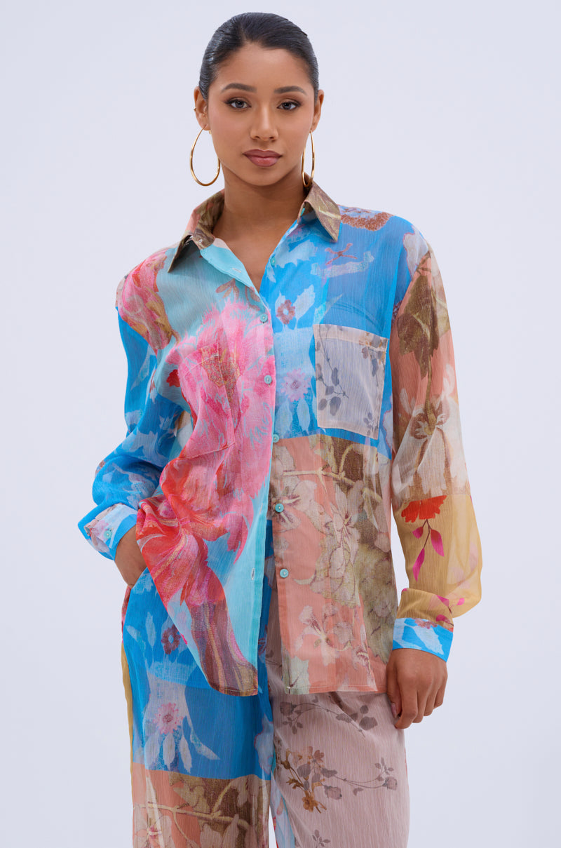 A woman with long dark hair in a ponytail, wearing large hoop earrings and the LILY CHIFFON BUTTON DOWN TOP with matching pants, stands against a plain light background.