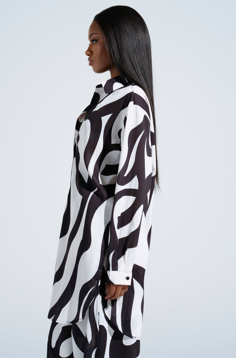 A person with long black hair stands in profile against a light gray background, exuding style in AKIRA's bold black and white abstract swirl pattern, featuring the LET IT GO BUTTON DOWN TOP and matching pants.