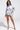 A woman exudes elegance in a floral-patterned jacket and shorts, highlighted with green trim, perfectly paired with a beige feathered purse and decorative heels, channeling the essence of the FLOWER PARTY SATIN BUTTON UP SHIRT.