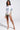 A person stands confidently in a FLOWER PARTY SATIN BUTTON UP SHIRT with matching shorts, holding a beige clutch adorned with feathers and wearing beige strappy heels, set against a plain background.