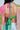 A woman with long dark hair wears the LOVE LOVE LOVE BLOUSE, a colorful chiffon open-back top with green, pink, and yellow patchwork bandana print, tied with bows at the neck and lower back, paired with light-wash denim jeans.