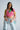 A woman in yellow sunglasses and the LOVE LOVE LOVE BLOUSE—a patchwork bandana print top in pink, green, and yellow—paired with light blue high-waisted jeans, poses confidently against a plain light gray background.