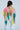 A person with long dark hair wears the LOVE LOVE LOVE BLOUSE—a colorful, backless halter top with a pink, yellow, and green patchwork bandana print—paired with light blue jeans against a plain light background.