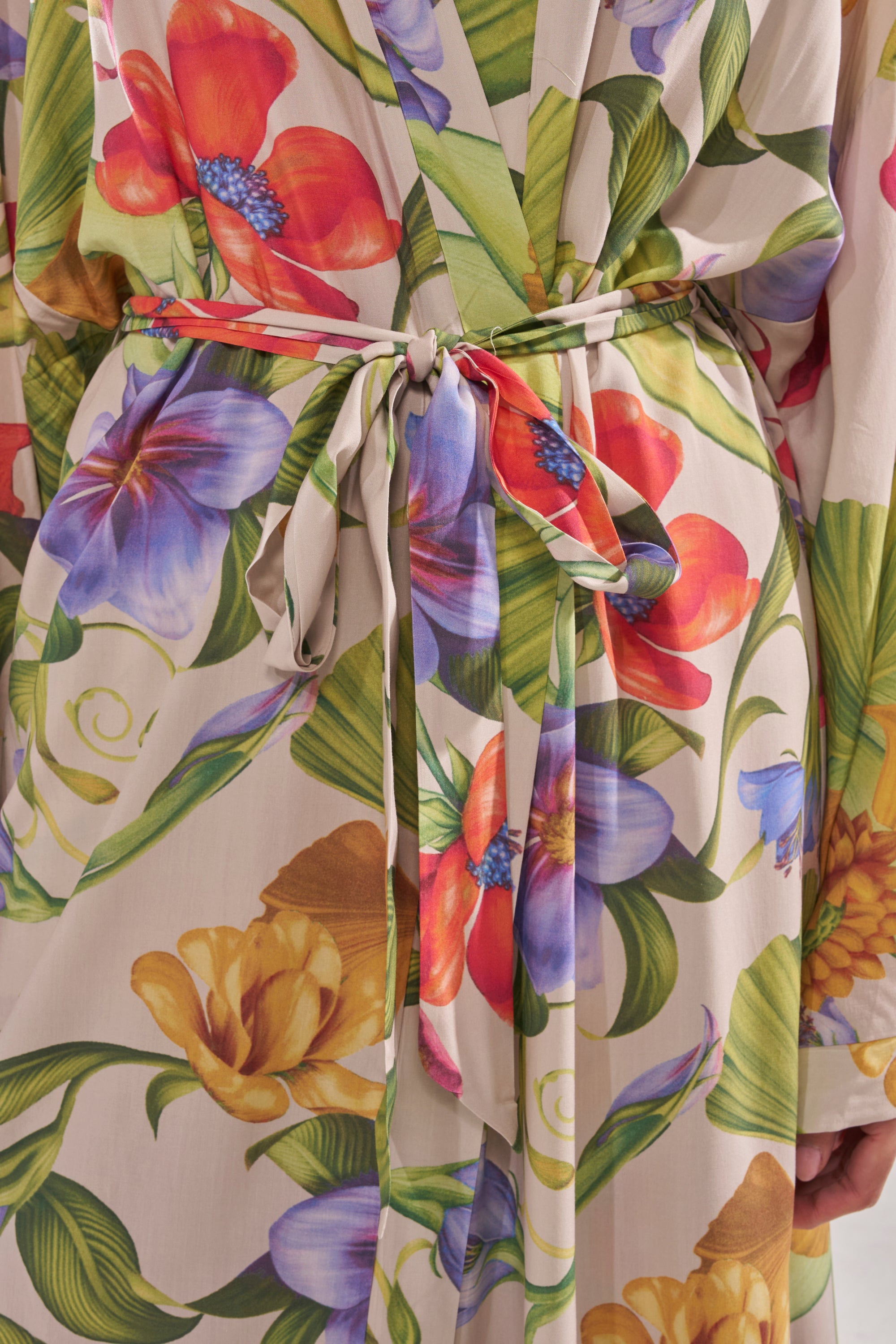 Close-up of the INTO THE GARDEN CARDIGAN, showcasing a vibrant floral pattern with red, yellow, purple, and blue blooms plus green leaves, tied at the waist with a matching belt. 7